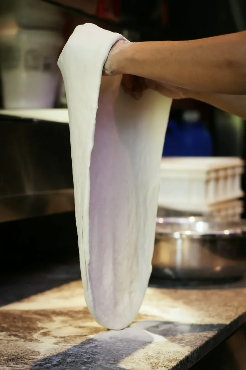 A NYPD Pizza 99 chef in a New York Department apron shaping a pizza behind the counter.
