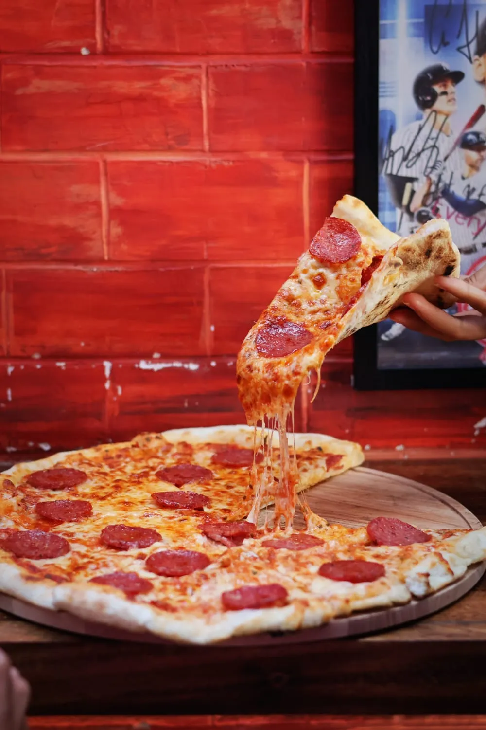 A wide slice of hot pizza being lifted, with long threads of melted mozzarella stretching down.