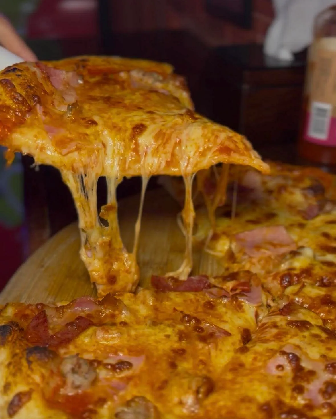 A wide slice of hot pizza being lifted, with long threads of melted mozzarella stretching down.